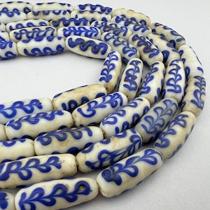 May include: A strand of white glass beads with blue leaf designs. The beads are cylindrical and have a slightly irregular shape.