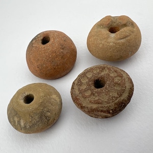 May include: Four terracotta clay pottery beads with holes in the center. The beads are different shapes and sizes. One bead has a decorative pattern.