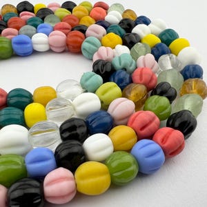 May include: A collection of colorful glass beads with a textured, flower-like design. The beads are arranged in a circular pattern, showcasing a variety of colors, including blue, green, yellow, red, and pink.