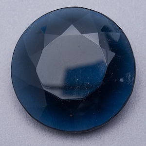 May include: A dark blue faceted glass button with a round shape.