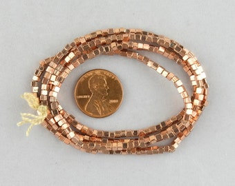 May include: A strand of rose gold square beads, approximately the size of a US penny.