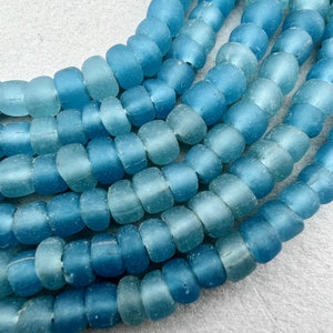 May include: A close-up of a strand of light blue glass beads. The beads are round and have a frosted finish. They are arranged in a staggered pattern, creating a visually appealing texture.