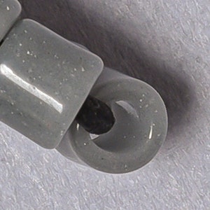 May include: A close-up of a gray plastic bead with a hole in the center. The bead is part of a string of beads.