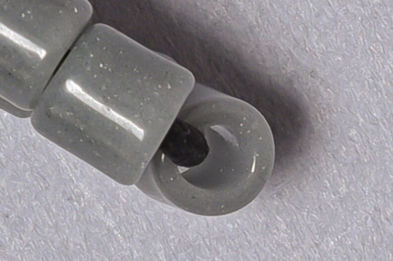 May include: A close-up of a gray plastic bead with a hole in the center. The bead is part of a string of beads.