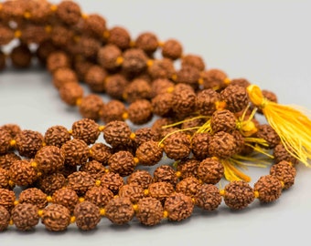 May include: Close-up of a strand of brown prayer beads, likely a mala, with a yellow tassel. The beads are round and textured, strung together with yellow thread. The background is a soft gray.