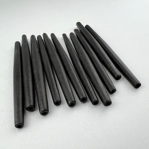 May include: A collection of dark brown, cylindrical wooden beads. Each bead has a tapered shape with a hole at one end. The beads are arranged on a white surface, showcasing their smooth, polished texture.