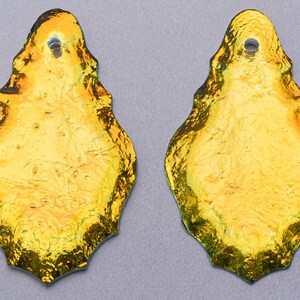 May include: Two gold-colored glass teardrop-shaped pendants with a hole at the top for hanging.