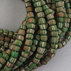 May include: A close-up of a strand of green, white, and orange striped glass beads. The beads are small and round, and they are arranged in a random pattern.