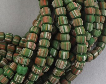 May include: A close-up of a strand of green, white and orange striped glass beads. The beads are small and round, and they are arranged in a random pattern.