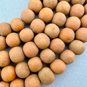 May include: A collection of smooth, light brown clay beads. The beads are round and have a slightly textured surface.