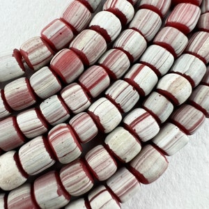 May include: A strand of white and red striped glass beads. The beads are cylindrical and have a slightly rounded shape. The beads are arranged in a staggered pattern.