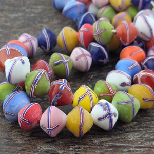 May include: A collection of multi-coloured glass beads, each featuring a distinct diamond-like shape with a smooth, glossy finish. The beads are decorated with a thin, raised cross pattern in blue and white, appearing in shades of red, yellow, green, blue, and white.
