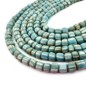 Puede incluir: Primer plano de un collar de cuentas a rayas azules y blancas. Las cuentas son cilíndricas con bordes redondeados y un acabado mate. La paleta de colores incluye tonos de azul y blanco, creando una estética vintage. Ideal para la creación de joyas.