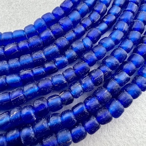 May include: A strand of cobalt blue glass beads with a frosted finish. The beads are round and have a slightly irregular shape.