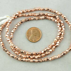 May include: A strand of rose gold colored faceted beads. The beads are approximately the size of a US penny.