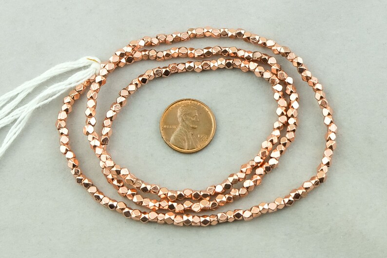 May include: A strand of rose gold colored faceted beads. The beads are approximately the size of a US penny.