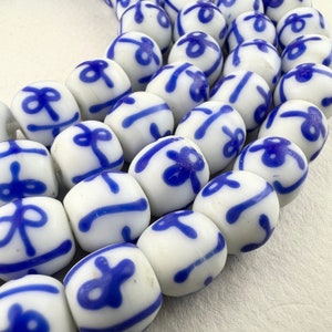 May include: A string of white ceramic beads with blue floral and geometric designs. The beads are round and have a glossy finish.