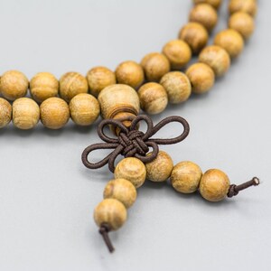 May include: A wooden beaded necklace with a brown knotted tassel. The beads are light brown and have a natural wood finish.