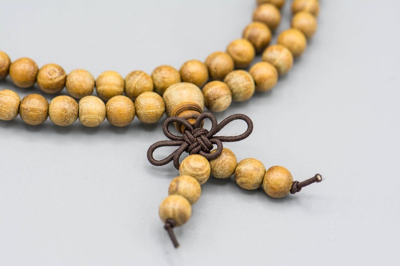 May include: A wooden beaded necklace with a brown knotted tassel. The beads are light brown and have a natural wood finish.