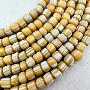 May include: A strand of yellow and white striped glass beads. The beads are round and have a smooth, polished finish.