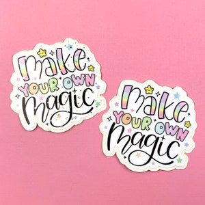 May include: Two white stickers with rainbow lettering that reads "Make your own magic" with small stars and glitter accents.