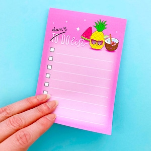May include: A rectangular pink notepad featuring the text "don't TO DO list" at the top. The design includes illustrations of a watermelon slice, a pineapple wearing heart-shaped sunglasses, and a coconut drink. It has six white checkboxes and lines.