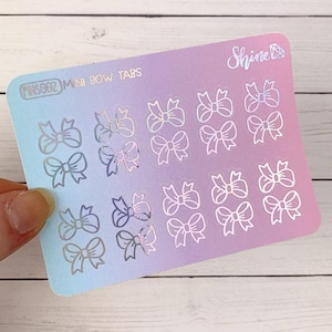 May include: A sheet of mini bow tabs stickers with a blue, purple, and pink gradient background. The stickers are silver and holographic. The text "MINI BOW TABS" and "Shine" are visible on the sticker sheet.