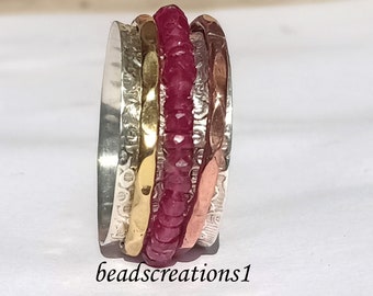 Könnte beinhalten: Ein mehrreihiger Ring mit einem zentralen Band aus kleinen, facettierten roten Edelsteinen. Der Ring hat Bänder aus Silber, Gold und kupferfarbenem Metall mit strukturierten Oberflächen. Der Text "beadscreations1" befindet sich unten.
