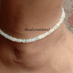 May include: A delicate white opal anklet with a silver clasp. The anklet is made of small, round opal beads that are strung together on a thin silver chain.