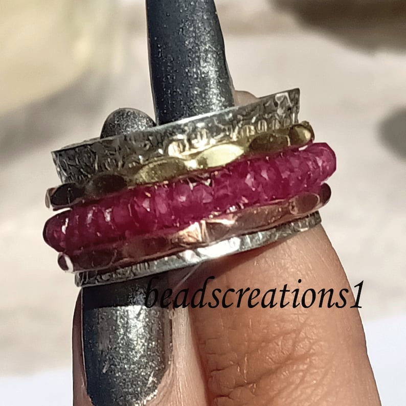 K&ouml;nnte beinhalten: Mehrere Ringe aus Silber und Gold, einer davon mit einem Band aus leuchtend rosa Edelsteinen. Die Ringe weisen strukturierte und geh&auml;mmerten Metalldetails auf. Der Text "beadscreations1" ist sichtbar.