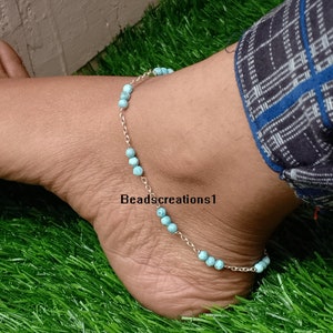 May include: A silver chain anklet with light blue beads. The anklet is on a person's ankle, with green grass in the background. The text "Beadscreations1" is visible on the ankle.