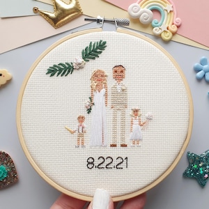 Puede incluir: Un bastidor de bordado de punto de cruz con una escena de boda con una novia, un novio y dos ni&ntilde;os. La fecha "8.22.21" est&aacute; bordada debajo de las figuras. El bordado est&aacute; en un bastidor de madera, con elementos decorativos alrededor.