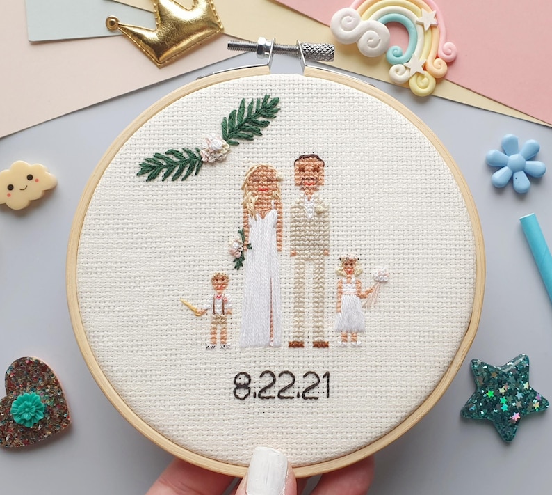 Puede incluir: Un bastidor de bordado de punto de cruz con una escena de boda con una novia, un novio y dos ni&ntilde;os. La fecha "8.22.21" est&aacute; bordada debajo de las figuras. El bordado est&aacute; en un bastidor de madera, con elementos decorativos alrededor.
