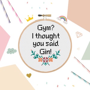 Könnte beinhalten: Ein weißer Stickrahmen mit dem Text "Gym? I thought you said Gin!" in schwarzer Schrift. Der Text ist von grünen Blättern und orangefarbenen Blumen umgeben.