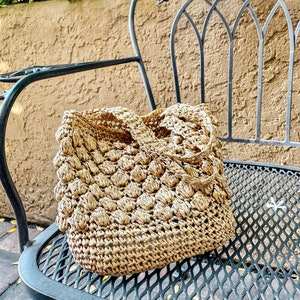 May include: A woven straw bag with a round, textured design. The bag is sitting on a black metal chair with a decorative grapevine design.