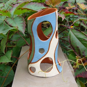 K&ouml;nnte beinhalten: Eine handgefertigte Keramikvase mit einem einzigartigen, offenen Design. Die Vase hat eine Kombination aus Farben, darunter Hellblau, Creme und Braun, mit einer Reihe von kreisf&ouml;rmigen Aussparungen. Die Vase ist etwa 20 cm hoch.