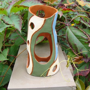 K&ouml;nnte beinhalten: Eine handgefertigte Keramikvase mit einem einzigartigen, offenen Design. Die Vase hat eine Mischung aus Farben, darunter Gr&uuml;n, Wei&szlig; und Blau, mit einem braunen Innenraum. Sie hat mehrere kreisf&ouml;rmige Aussparungen und ist etwa 25 cm hoch.
