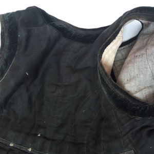 May include: Black sleeveless garment with a velvet trim. The garment is made of a thick fabric and has a gathered skirt.