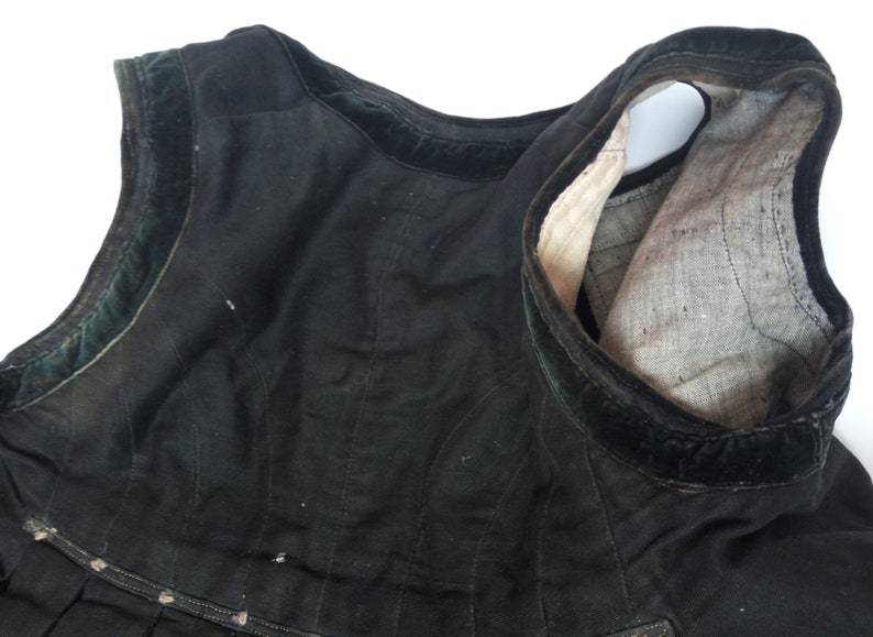 May include: Black sleeveless garment with a velvet trim. The garment is made of a thick fabric and has a gathered skirt.