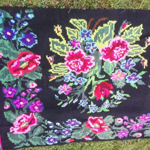 May include: A black wool rug with a floral design. The rug features pink, red, green, and blue flowers on a black background.