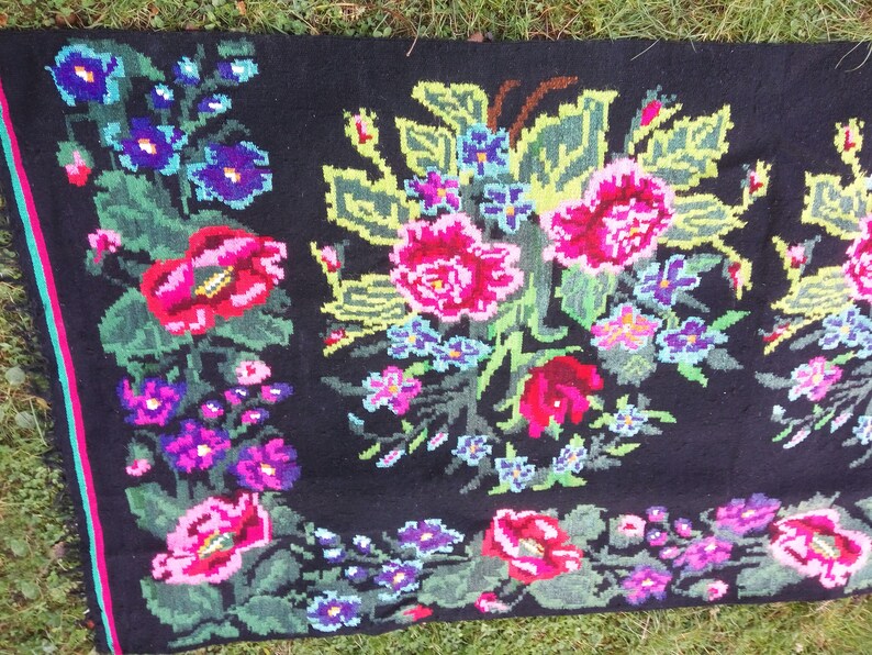 May include: A black wool rug with a floral design. The rug features pink, red, green, and blue flowers on a black background.