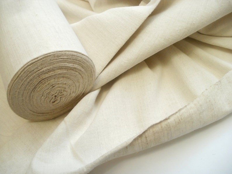 May include: A roll of natural-colored fabric, unbleached and woven, with a soft, textured surface. The fabric is folded and rolled, showing the raw edge.