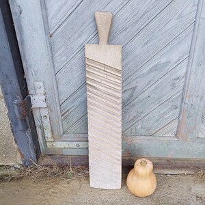May include: A wooden dough roller with a textured surface. The roller is light brown and has a handle on the top. It is standing on a wooden surface.
