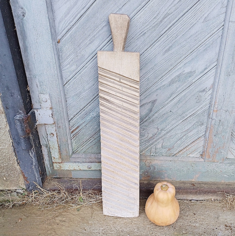 May include: A wooden dough roller with a textured surface. The roller is light brown and has a handle on the top. It is standing on a wooden surface.