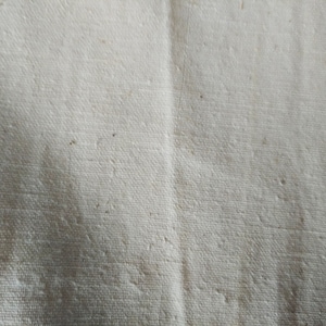 May include: Close-up of a white fabric with a textured weave. The fabric has a slightly off-white color and a subtle sheen.