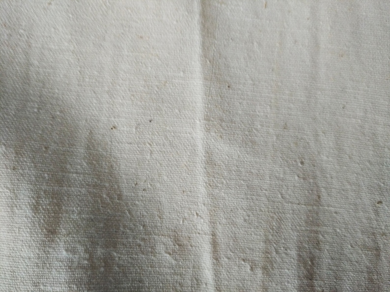May include: Close-up of a white fabric with a textured weave. The fabric has a slightly off-white color and a subtle sheen.
