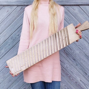 May include: A wooden washboard with a light brown color and a textured surface. The washboard has a handle on the right side.