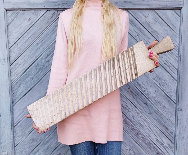 May include: A wooden washboard with a light brown color and a textured surface. The washboard has a handle on the right side.