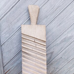 May include: A wooden washboard with a handle and a textured surface. The washboard is light brown and has a worn look.