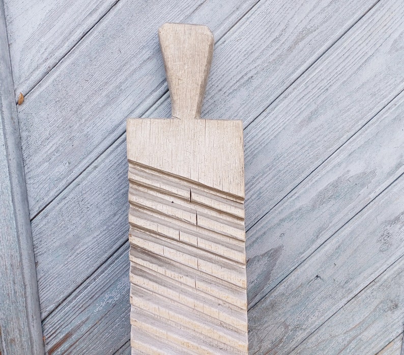 May include: A wooden washboard with a handle and a textured surface. The washboard is light brown and has a worn look.